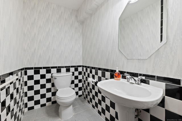 half bathroom featuring tile patterned flooring, tile walls, toilet, and a sink