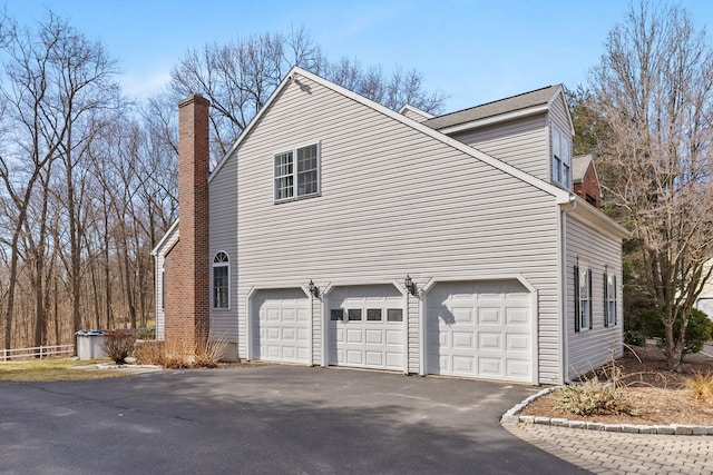 view of property exterior featuring aphalt driveway, an attached garage, and a chimney