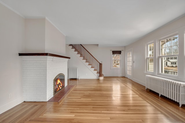 unfurnished living room featuring stairway, a brick fireplace, radiator heating unit, and baseboards