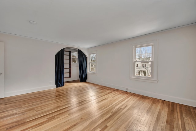 spare room with baseboards, arched walkways, plenty of natural light, and light wood finished floors