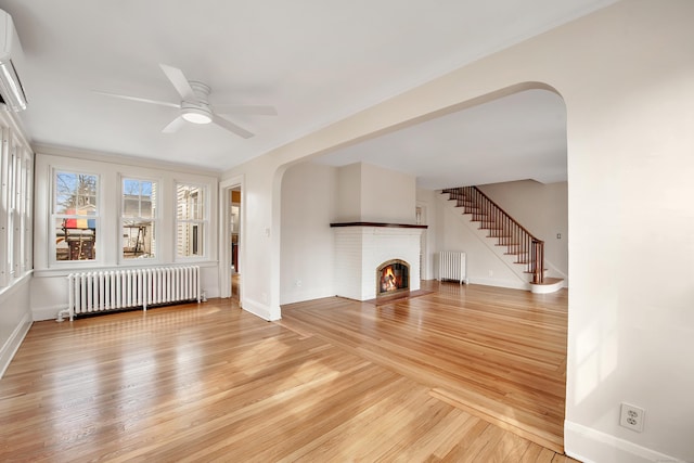 unfurnished living room featuring stairway, arched walkways, radiator heating unit, and light wood finished floors