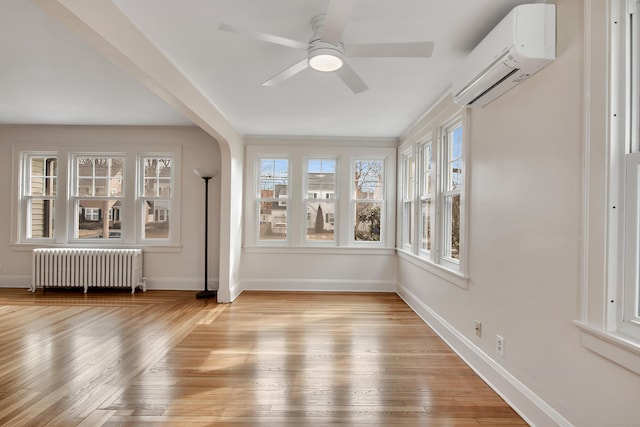 unfurnished sunroom with arched walkways, radiator, an AC wall unit, and a ceiling fan