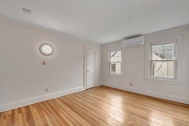 spare room featuring light wood-type flooring, baseboards, and a wall unit AC