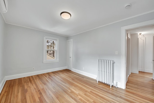 empty room with radiator, crown molding, baseboards, a wall mounted air conditioner, and light wood-type flooring