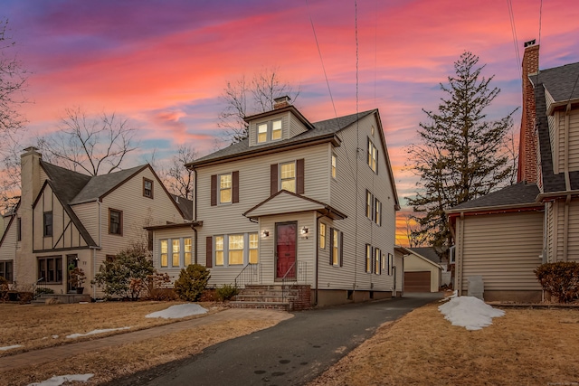 traditional style home with a garage, an outbuilding, a chimney, and aphalt driveway