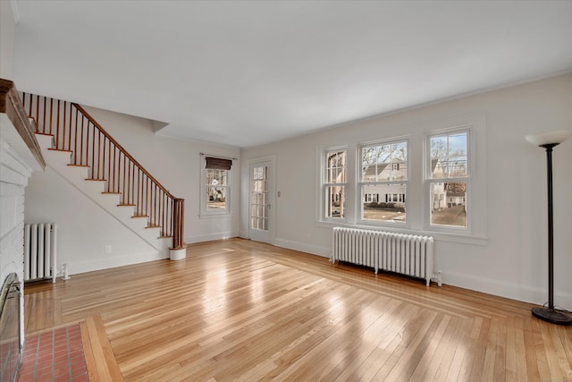 unfurnished living room with stairway, radiator heating unit, light wood-style floors, and baseboards