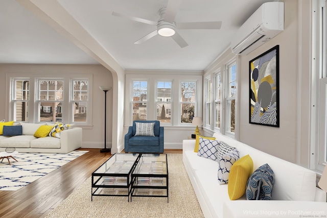 living area with an AC wall unit, wood finished floors, arched walkways, baseboards, and ceiling fan