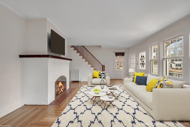 living area featuring baseboards, radiator heating unit, stairs, crown molding, and a brick fireplace