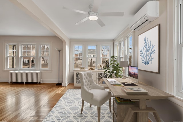 office area with baseboards, light wood finished floors, radiator heating unit, ceiling fan, and an AC wall unit