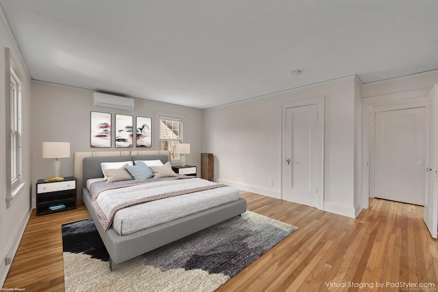 bedroom with baseboards, light wood-style flooring, and a wall mounted AC