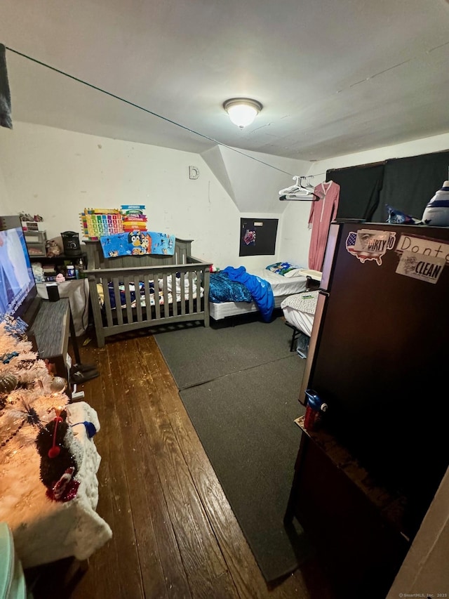 bedroom with vaulted ceiling, wood finished floors, and freestanding refrigerator