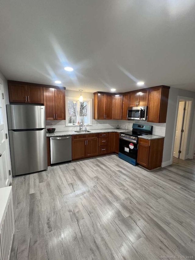 kitchen with stainless steel appliances, a sink, light wood-type flooring, decorative backsplash, and radiator