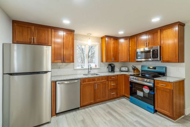 kitchen featuring a sink, decorative backsplash, brown cabinets, light stone countertops, and appliances with stainless steel finishes