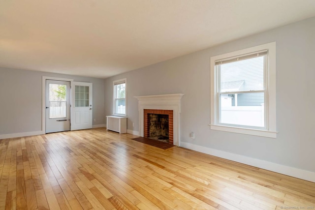 unfurnished living room featuring baseboards, a fireplace, light wood-style floors, and radiator