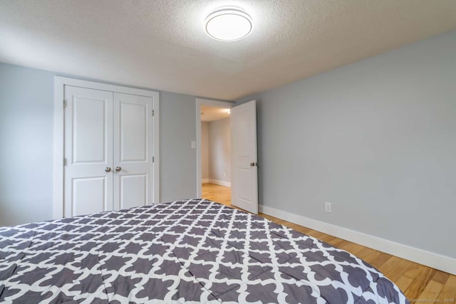 bedroom featuring a closet, wood finished floors, a textured ceiling, and baseboards