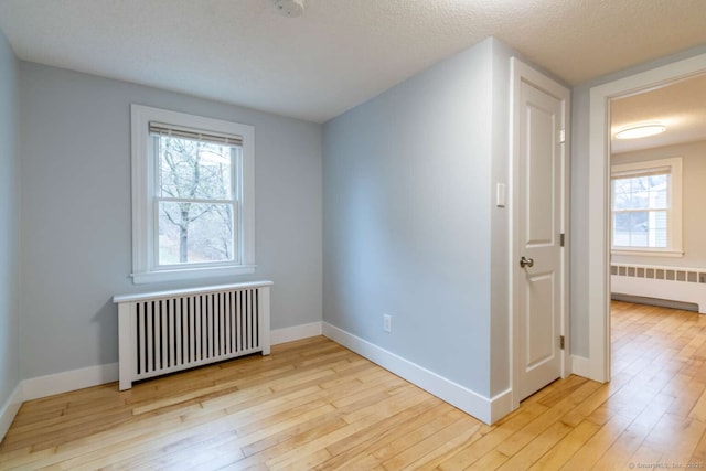 spare room with radiator heating unit, baseboards, and light wood-style floors