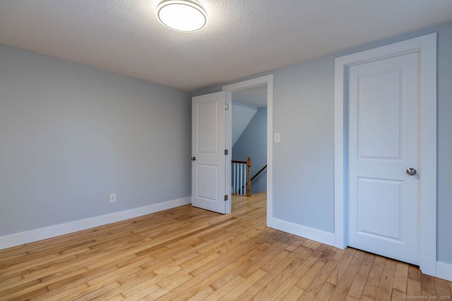 unfurnished room featuring light wood-type flooring, baseboards, and a textured ceiling