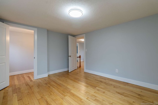 unfurnished room with light wood-style flooring, a textured ceiling, and baseboards
