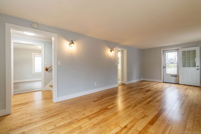unfurnished living room featuring stairway, baseboards, and light wood-style flooring