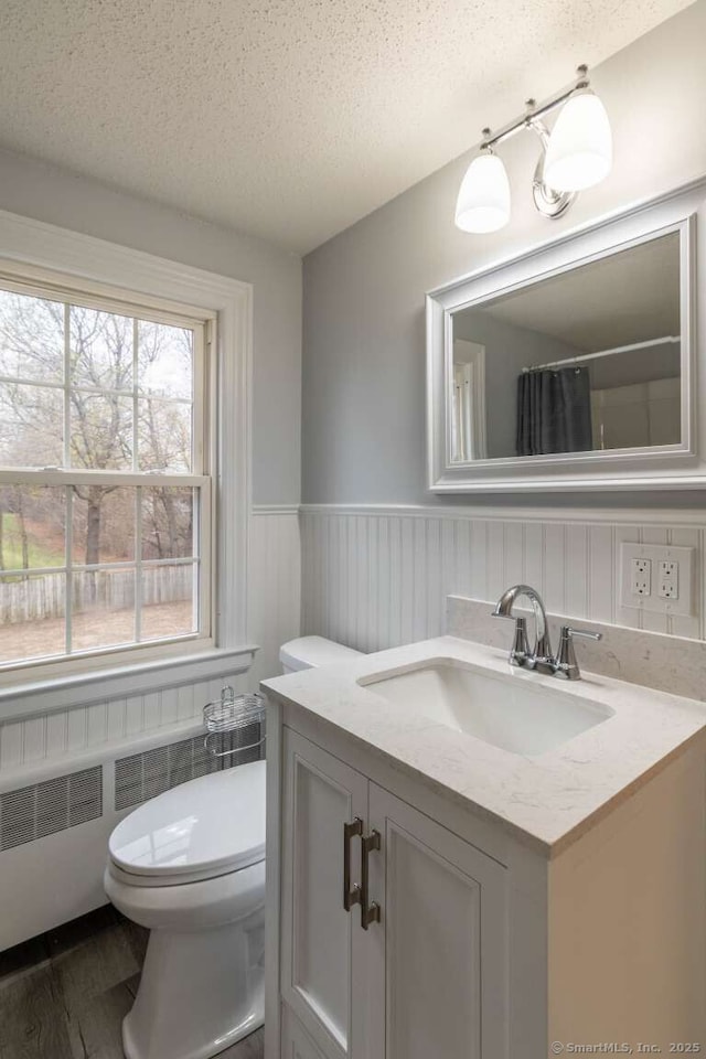 bathroom with a textured ceiling, toilet, wainscoting, wood finished floors, and vanity