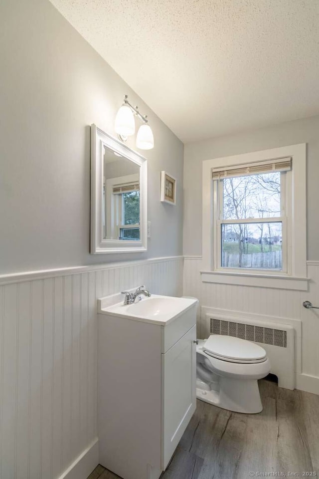 bathroom with radiator, a wainscoted wall, wood finished floors, toilet, and a textured ceiling