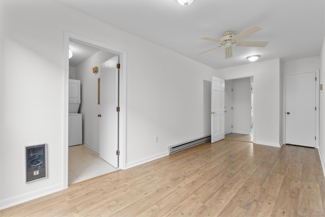 unfurnished room with light wood finished floors, a baseboard heating unit, ceiling fan, stacked washer and dryer, and heating unit