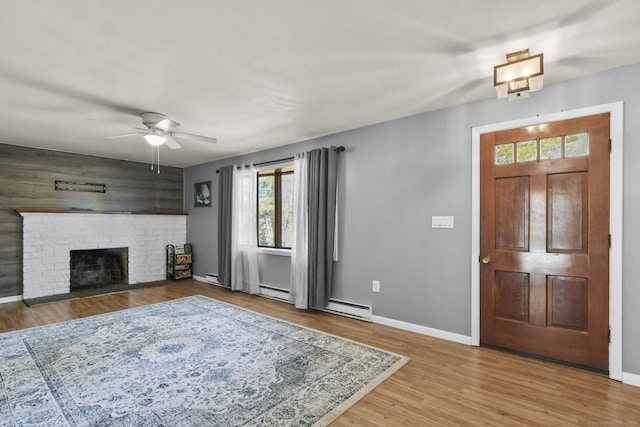 foyer with ceiling fan, baseboards, baseboard heating, a fireplace, and wood finished floors