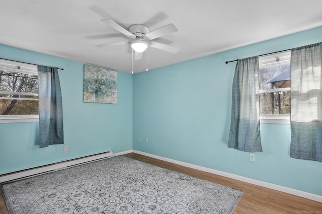 spare room featuring a healthy amount of sunlight, a baseboard heating unit, baseboards, and wood finished floors