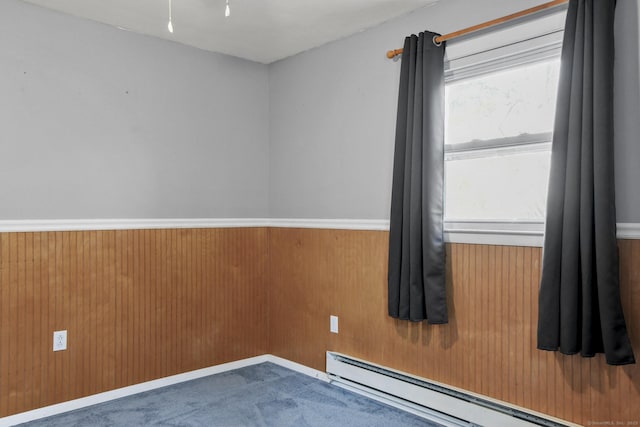 empty room with plenty of natural light, wood walls, baseboard heating, and wainscoting