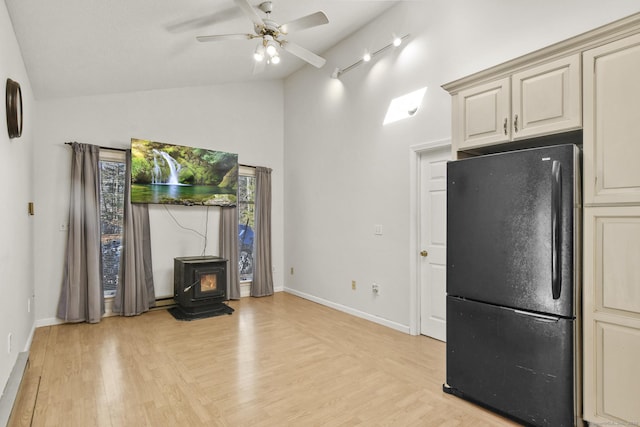 kitchen with cream cabinets, freestanding refrigerator, a wood stove, and vaulted ceiling