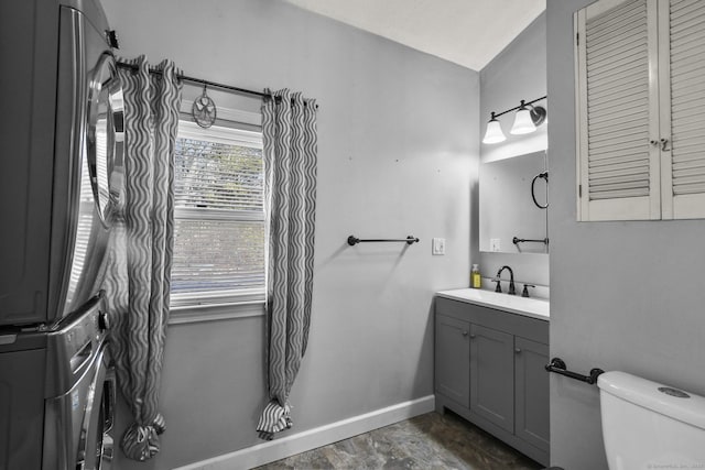 bathroom featuring vanity, toilet, baseboards, and stacked washer and clothes dryer