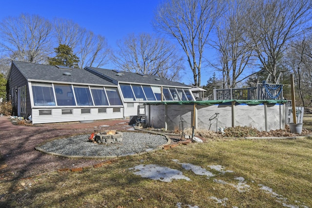 rear view of house featuring a covered pool, a shingled roof, a sunroom, and an outdoor fire pit