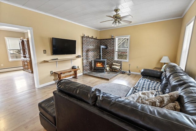 living area with a baseboard heating unit, ornamental molding, a wood stove, wood finished floors, and a ceiling fan