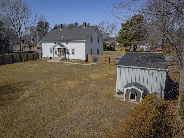 back of house with an outdoor structure, fence, a lawn, and a chimney