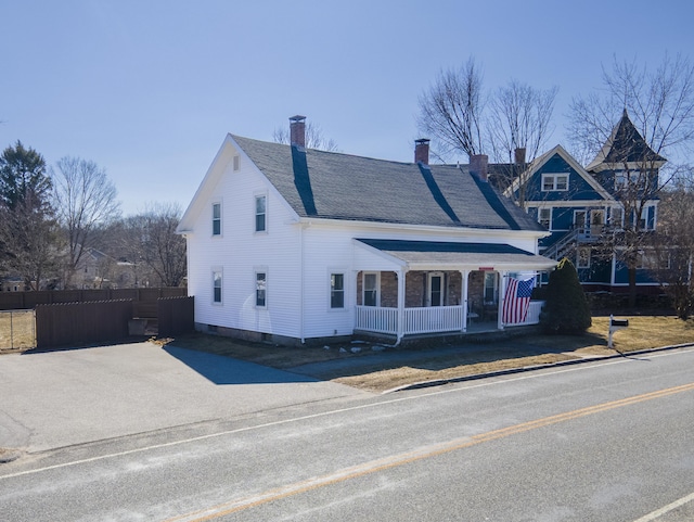 view of front of house with a chimney, a porch, a shingled roof, and fence