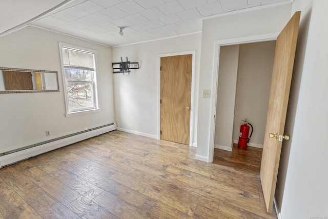 interior space featuring a baseboard heating unit, baseboards, ornamental molding, and hardwood / wood-style flooring