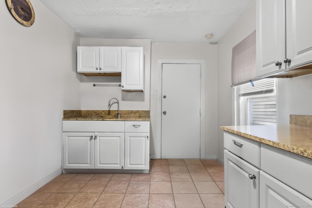 kitchen with a sink, baseboards, white cabinets, and light tile patterned floors