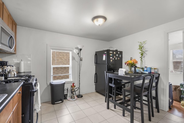 kitchen with stainless steel microwave, brown cabinets, freestanding refrigerator, and gas range