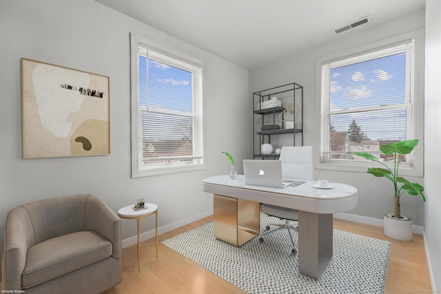 home office with a wealth of natural light, visible vents, baseboards, and wood finished floors