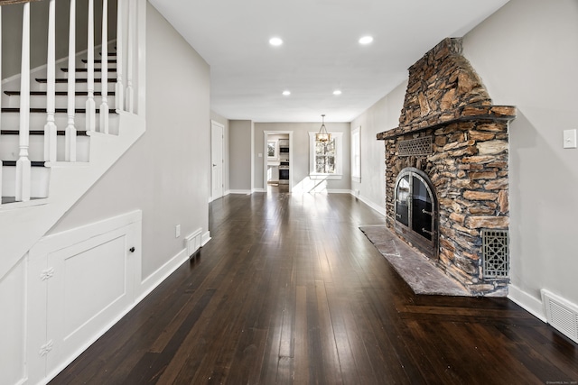 unfurnished living room with visible vents, baseboards, stairs, hardwood / wood-style floors, and a stone fireplace