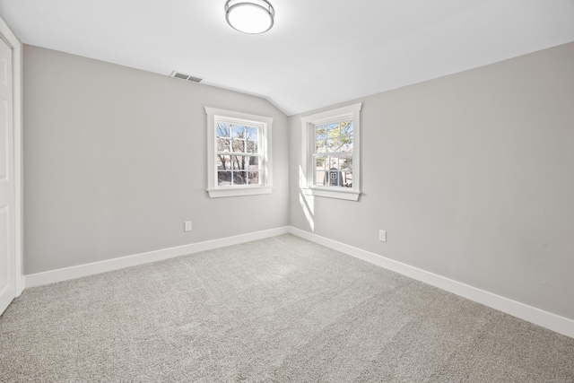 empty room featuring lofted ceiling, carpet, visible vents, and baseboards