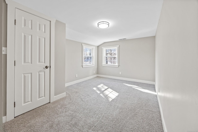 carpeted spare room with lofted ceiling, baseboards, and visible vents