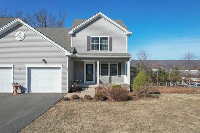 traditional-style home with driveway, an attached garage, roof with shingles, and a front yard