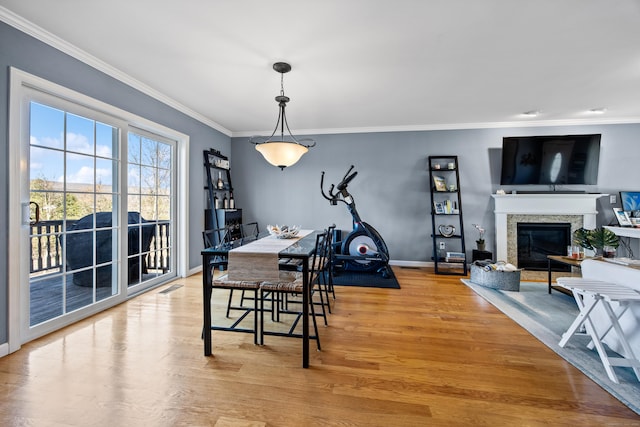 dining space with a glass covered fireplace, crown molding, visible vents, and light wood finished floors