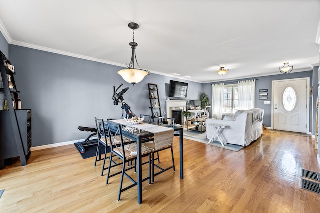 dining area featuring baseboards, light wood-style floors, a glass covered fireplace, and ornamental molding