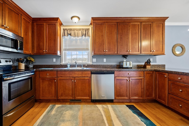 kitchen featuring a sink, crown molding, light wood finished floors, and stainless steel appliances