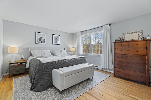 bedroom featuring light wood finished floors, baseboard heating, and baseboards