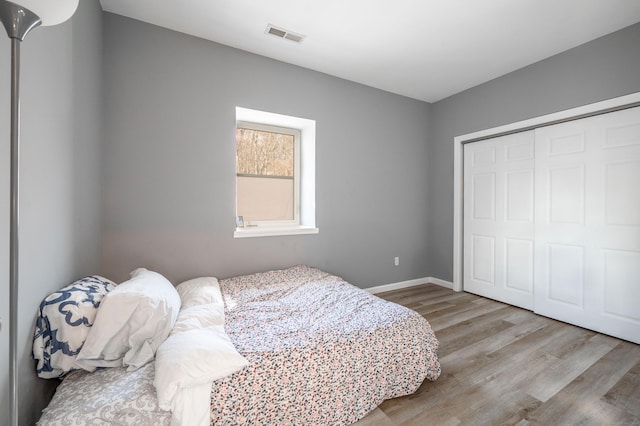 bedroom with a closet, visible vents, baseboards, and wood finished floors