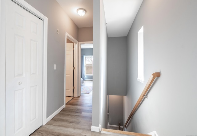 hallway with an upstairs landing, light wood-type flooring, and baseboards