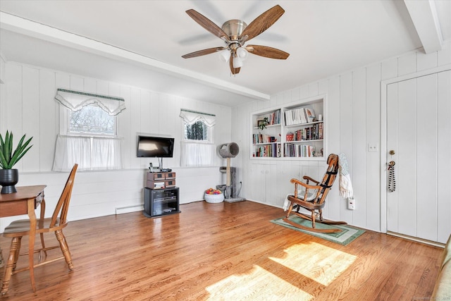 living area with light wood-style flooring, built in features, a ceiling fan, and beamed ceiling